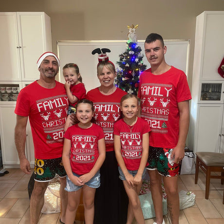 Family of five wearing matching red Christmas-themed t-shirts in a kitchen.