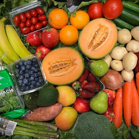 Assorted fruits, vegetables, and baby spinach on a green leafy background