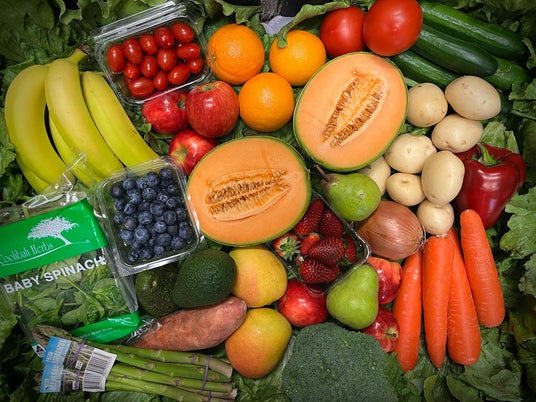 Assorted fruits, vegetables, and baby spinach on a green leafy background